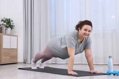 Photo of Woman doing plank exercise on fitness mat at home