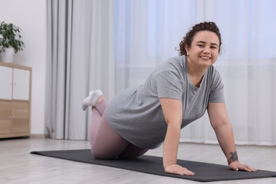 Plus size woman exercising on fitness mat at home