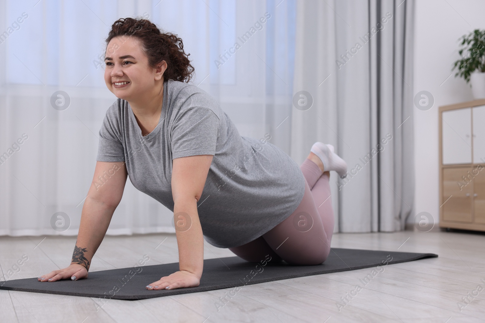 Photo of Plus size woman exercising on fitness mat at home