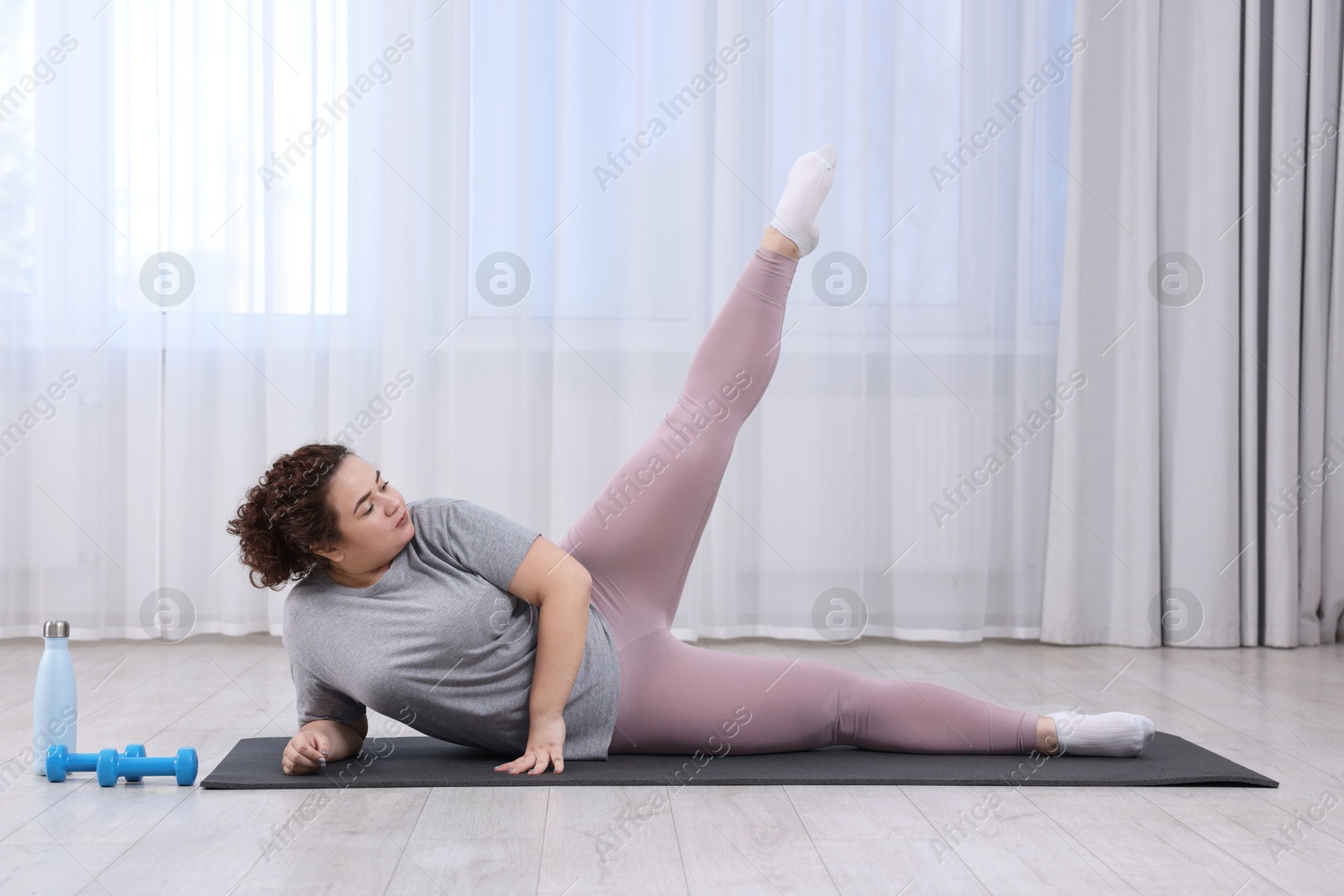 Photo of Plus size woman exercising on fitness mat at home