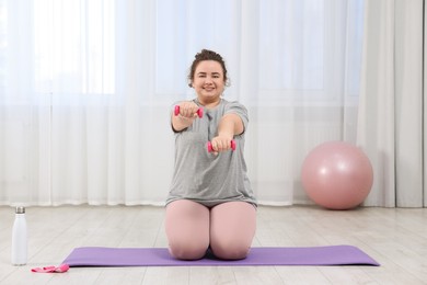 Photo of Plus size woman with dumbbells training at home