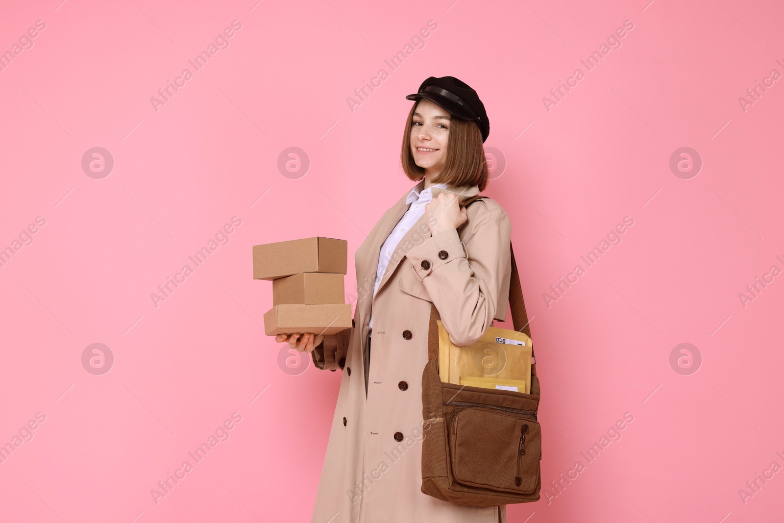 Photo of Happy postwoman with bag and parcels on pink background