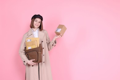 Photo of Happy postwoman with bag and parcel on pink background. Space for text