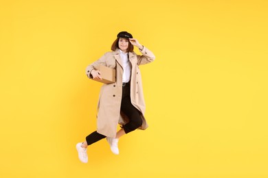 Photo of Happy postwoman with parcel jumping on yellow background. Space for text