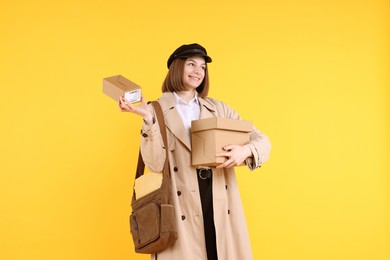 Photo of Happy postwoman with bag and parcels on yellow background