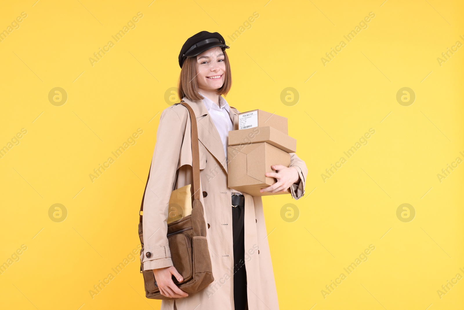 Photo of Happy postwoman with bag and parcels on yellow background