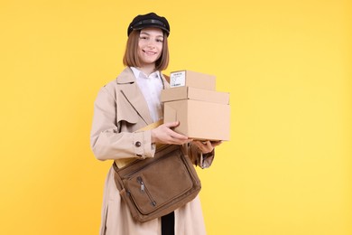 Photo of Happy postwoman with bag and parcels on yellow background