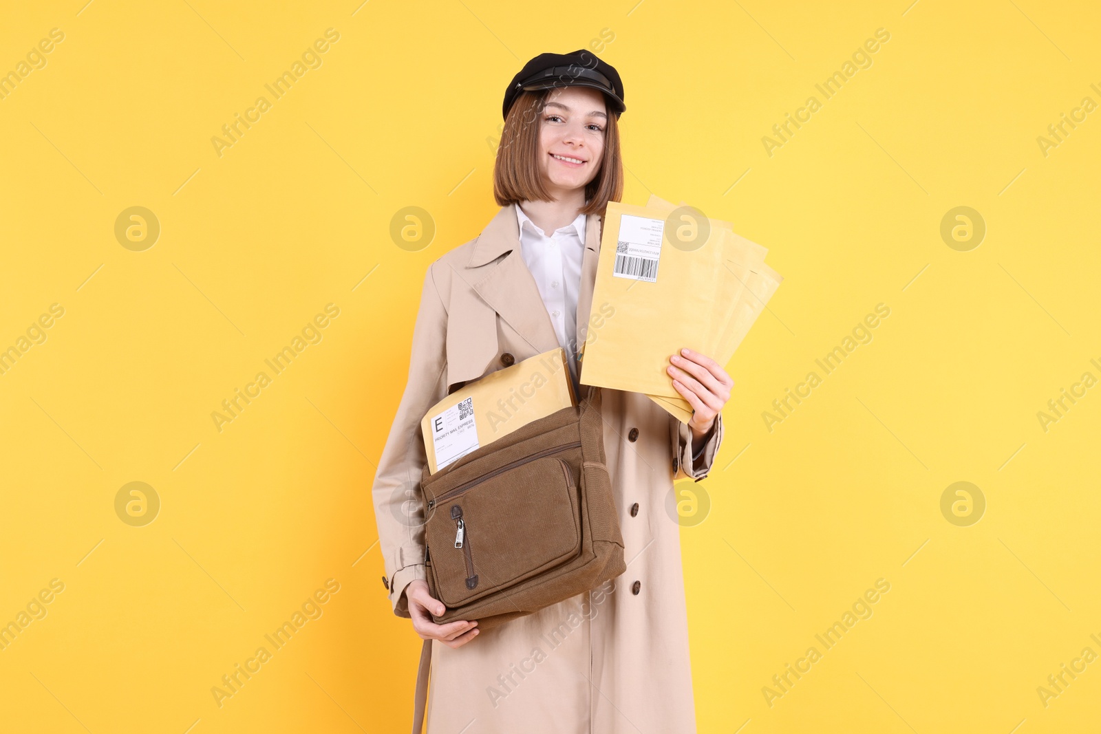 Photo of Happy postwoman with bag and envelopes on yellow background