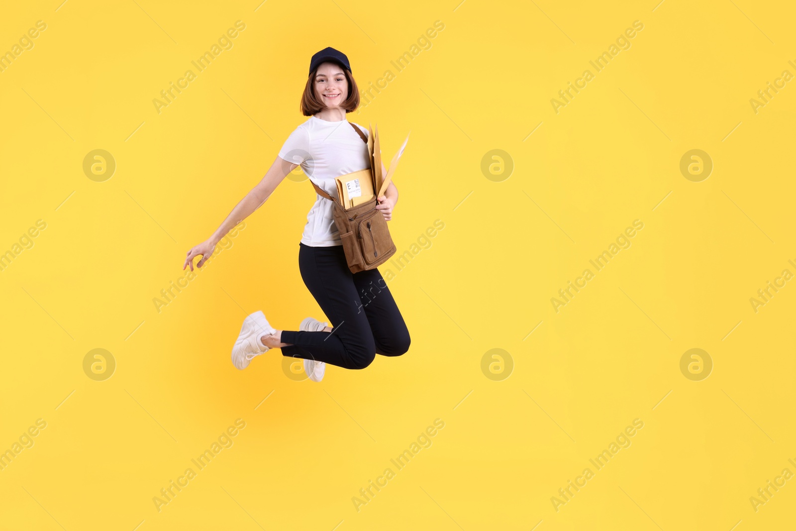 Photo of Happy postwoman with bag and envelopes jumping on yellow background. Space for text