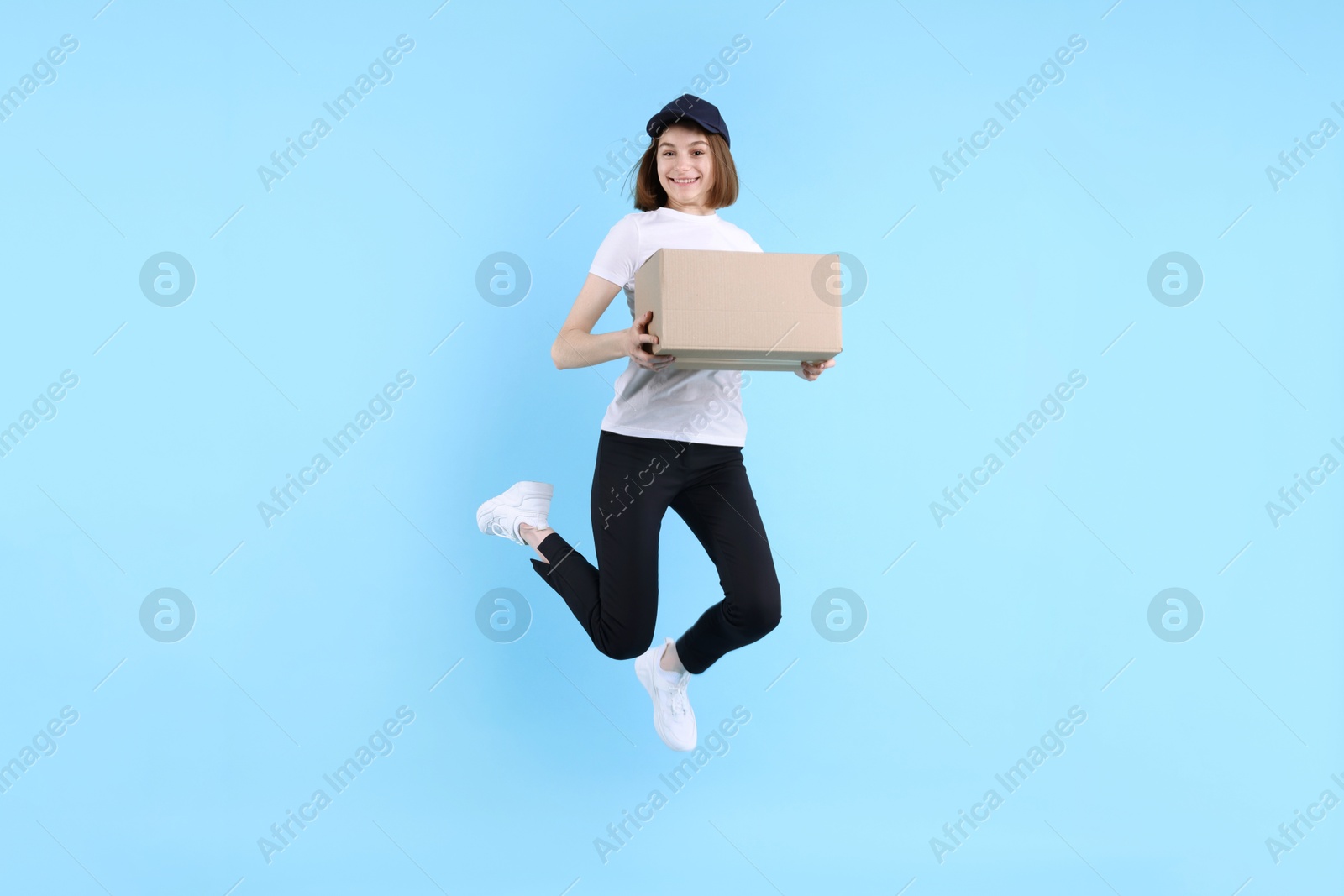 Photo of Happy postwoman with parcel jumping on light blue background