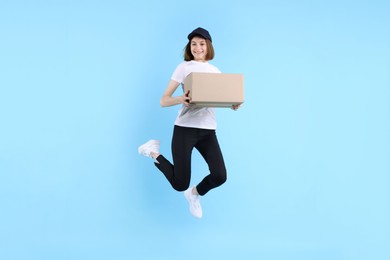 Photo of Happy postwoman with parcel jumping on light blue background