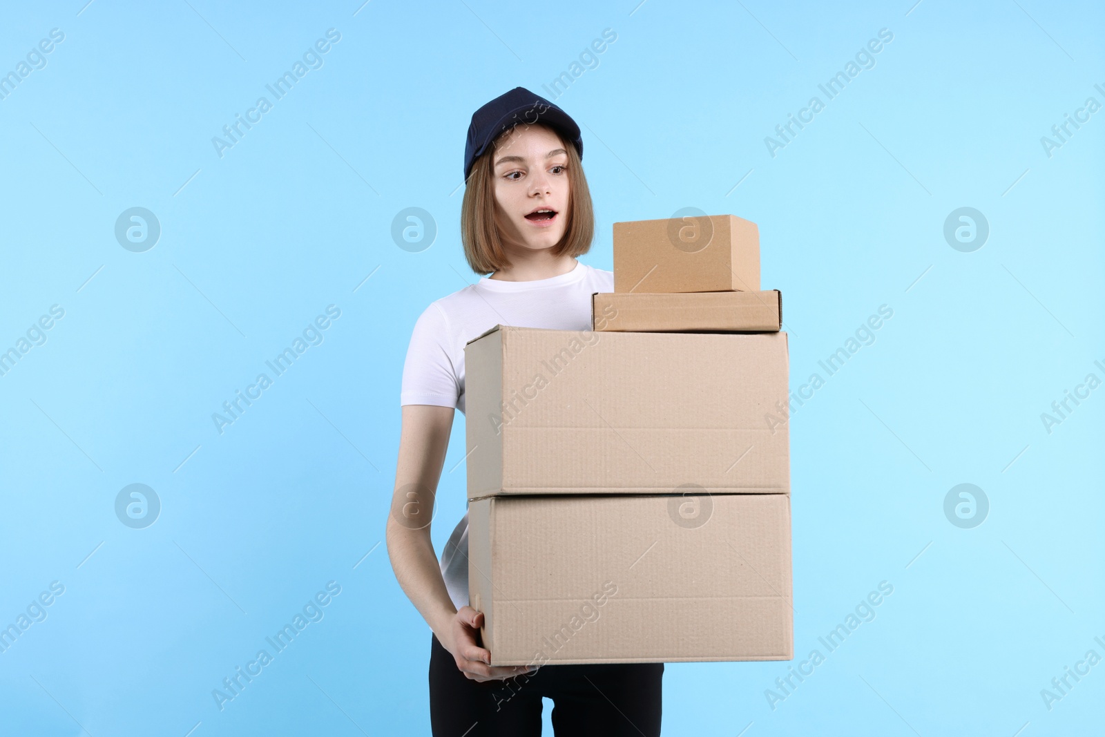 Photo of Emotional postwoman with parcels on light blue background