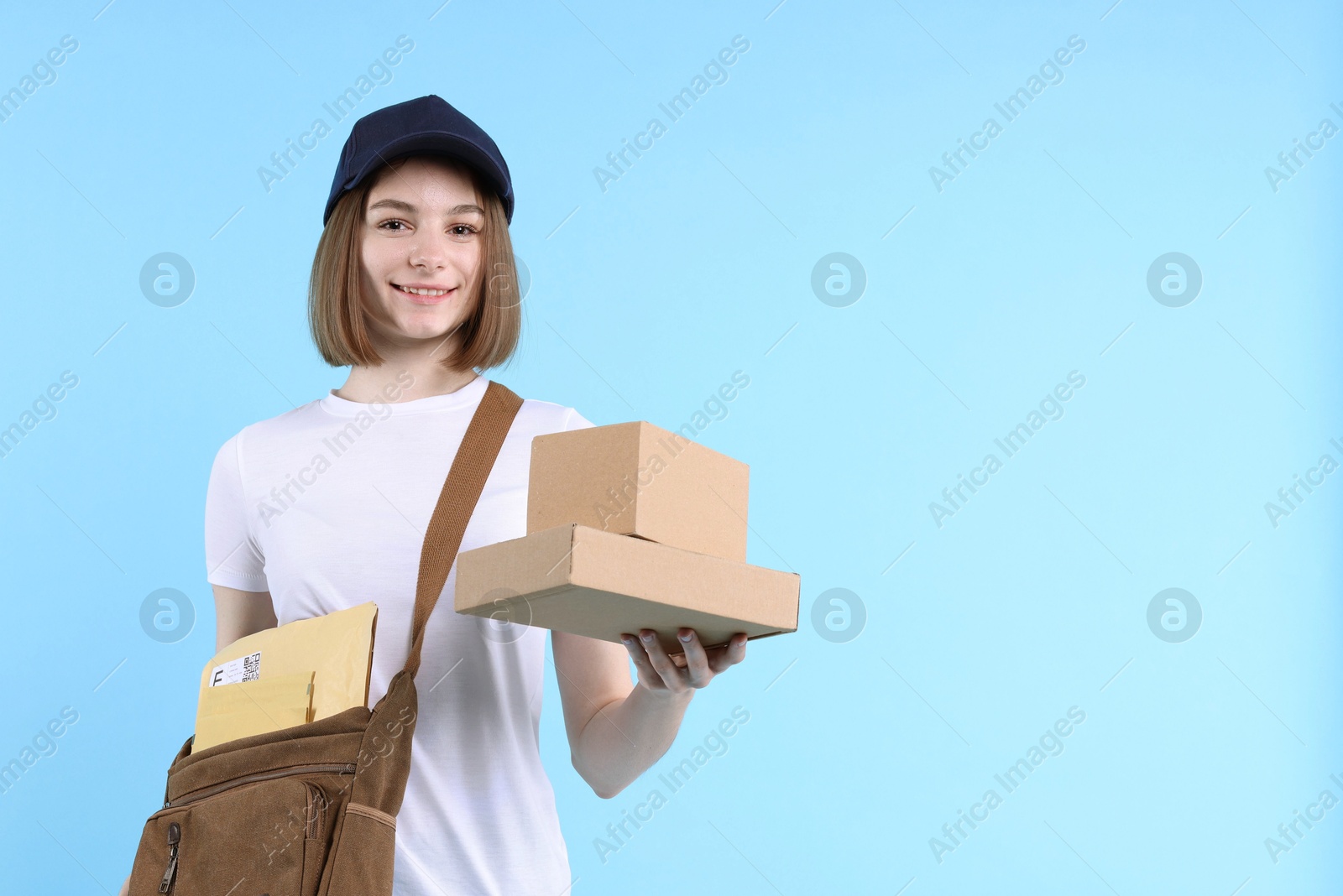 Photo of Happy postwoman with bag and parcels on light blue background. Space for text