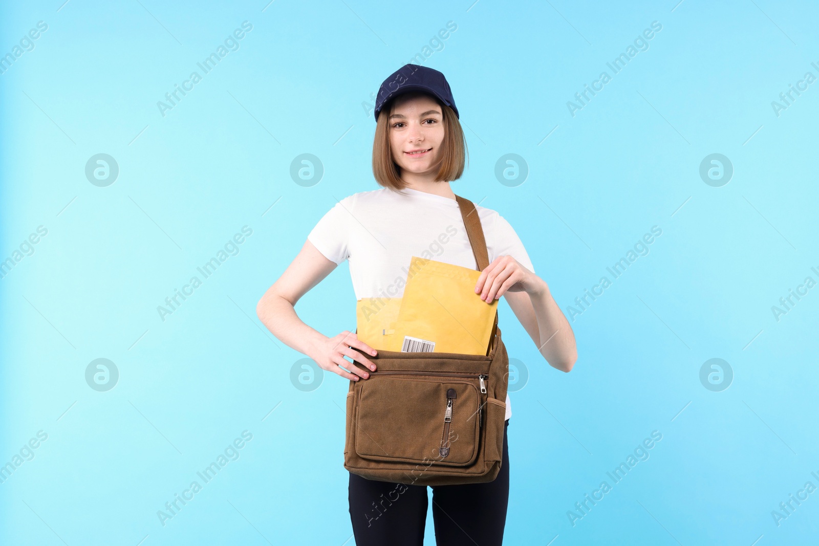 Photo of Happy postwoman with bag and envelopes on light blue background