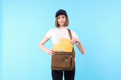 Photo of Happy postwoman with bag and envelopes on light blue background