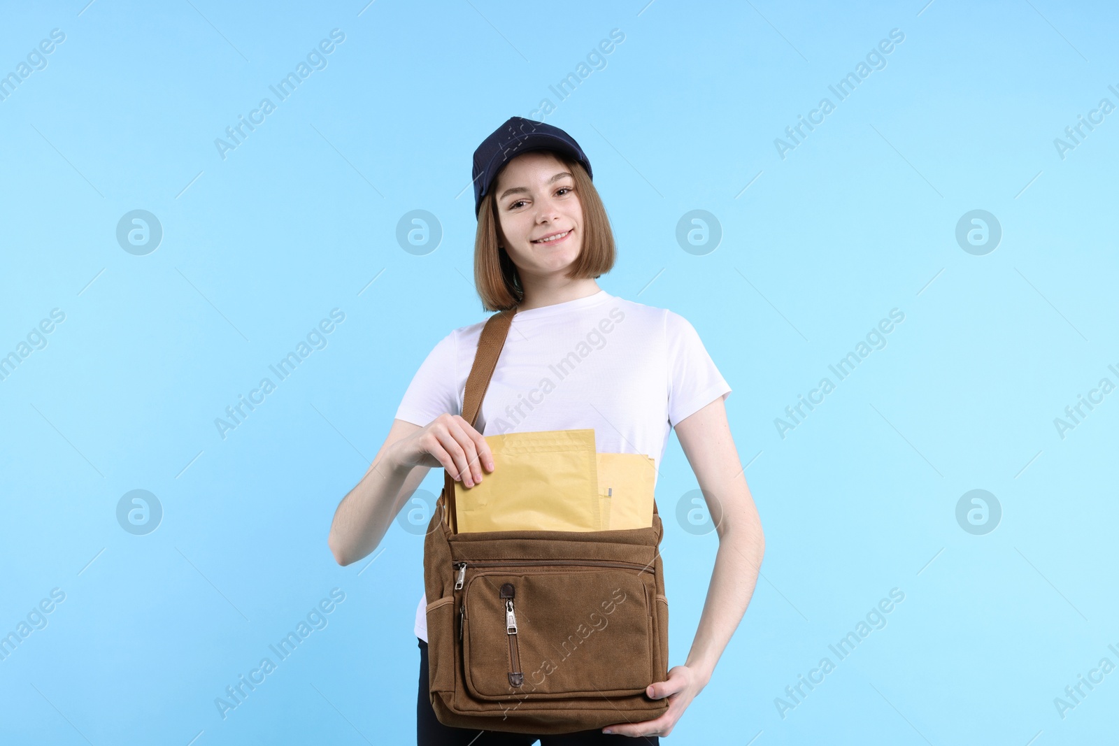 Photo of Happy postwoman with bag and envelopes on light blue background