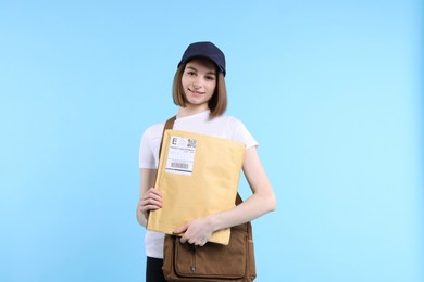 Photo of Happy postwoman with bag and envelopes on light blue background