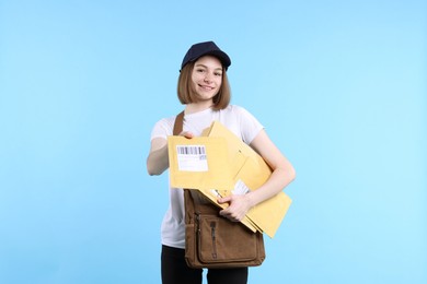 Photo of Happy postwoman with bag giving envelope on light blue background