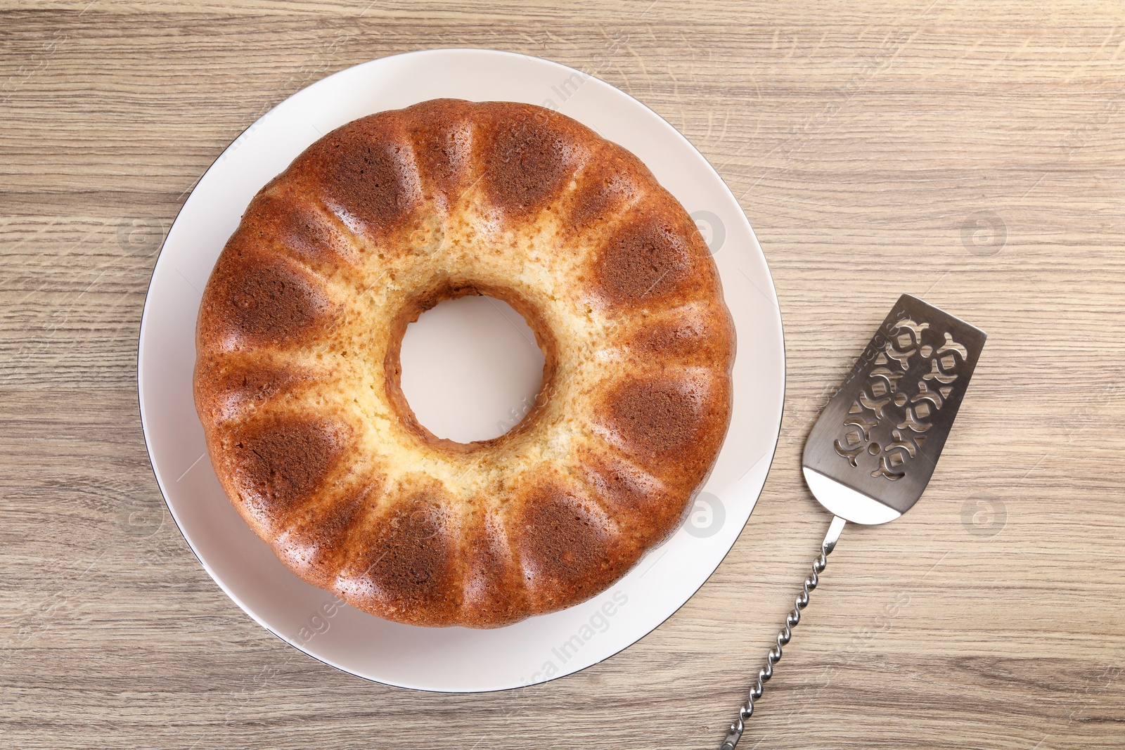 Photo of Freshly baked sponge cake and server on wooden table, top view