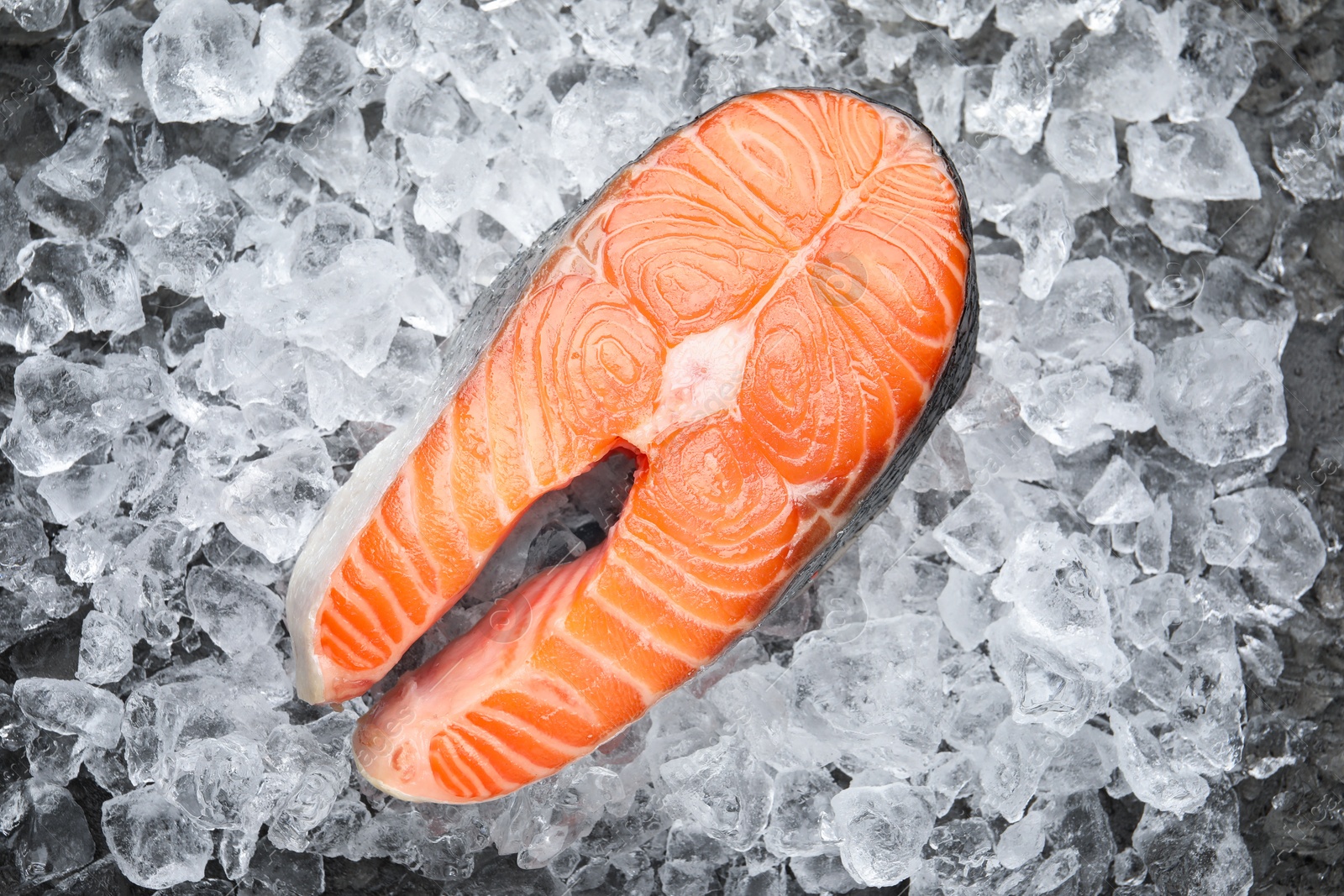 Photo of Fresh raw salmon steak on ice pieces, top view