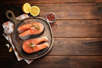 Photo of Fresh raw salmon steaks and spices on wooden table, flat lay. Space for text