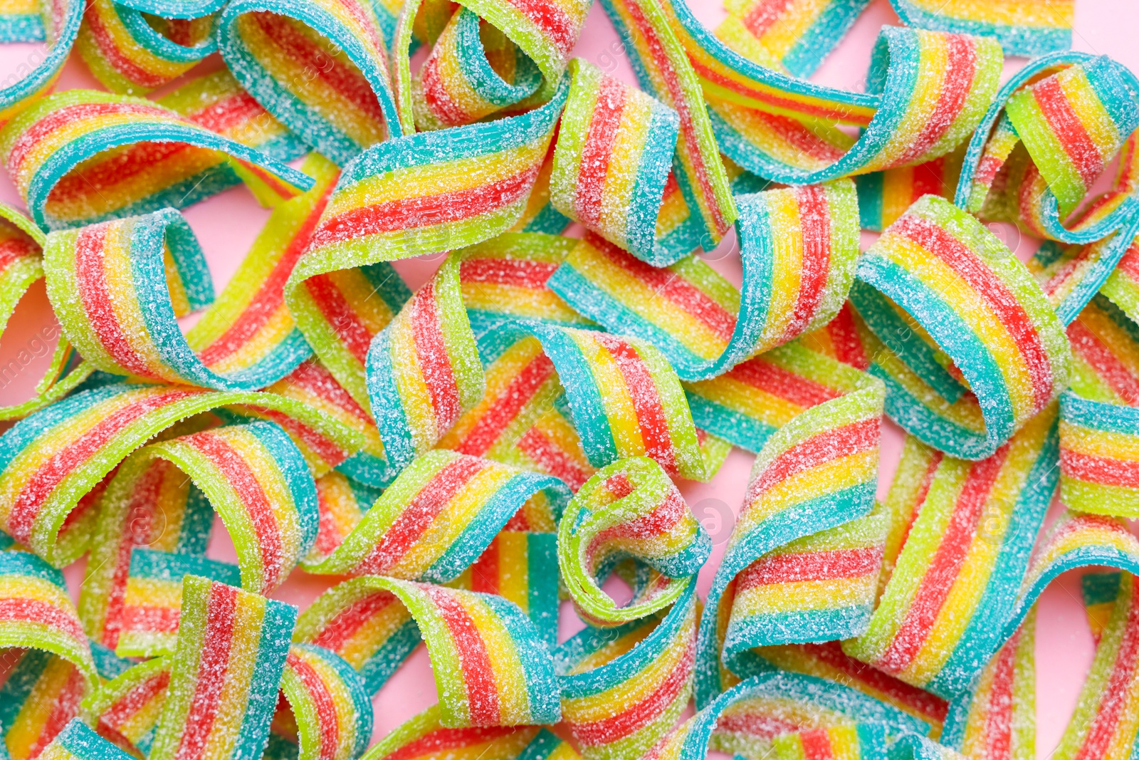 Photo of Tasty rainbow sour belts on pink background, top view