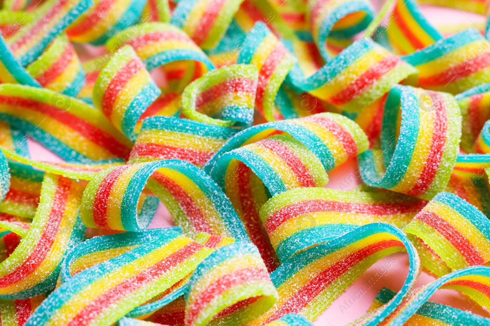 Photo of Tasty rainbow sour belts on pink background, closeup