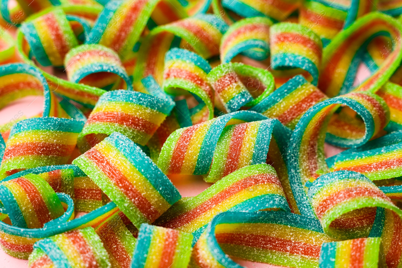 Photo of Tasty rainbow sour belts on pink background, closeup