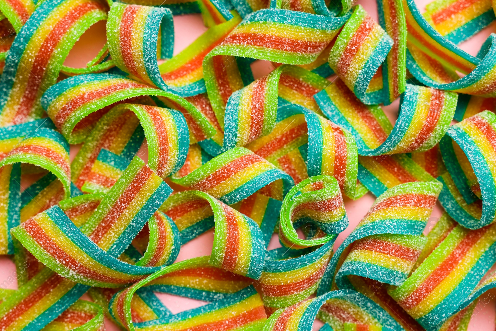 Photo of Tasty rainbow sour belts on pink background, top view