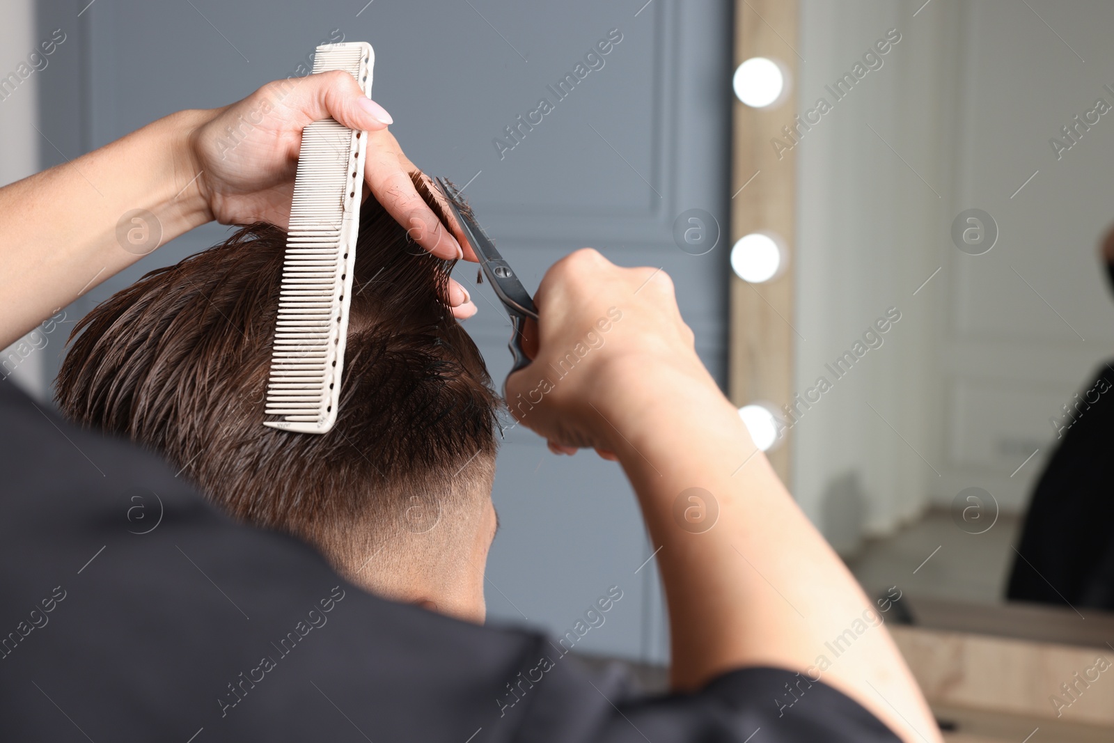 Photo of Professional hairdresser cutting client's hair with scissors in barbershop, closeup