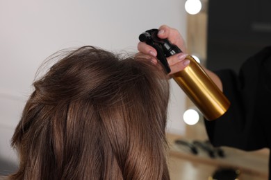 Photo of Hairdresser using spray while making stylish haircut in salon, closeup