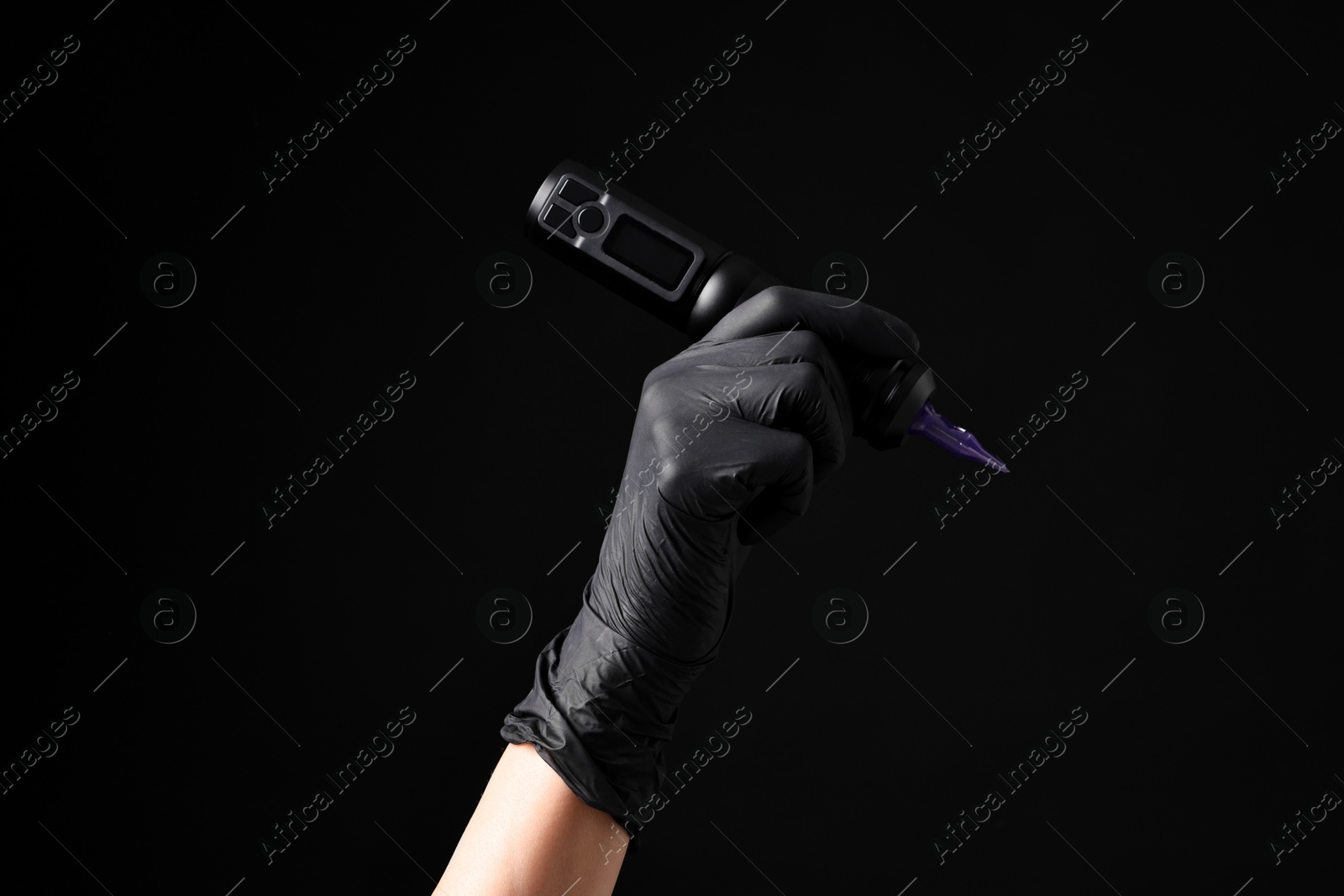 Photo of Professional artist in gloves holding tattoo machine on black background, closeup