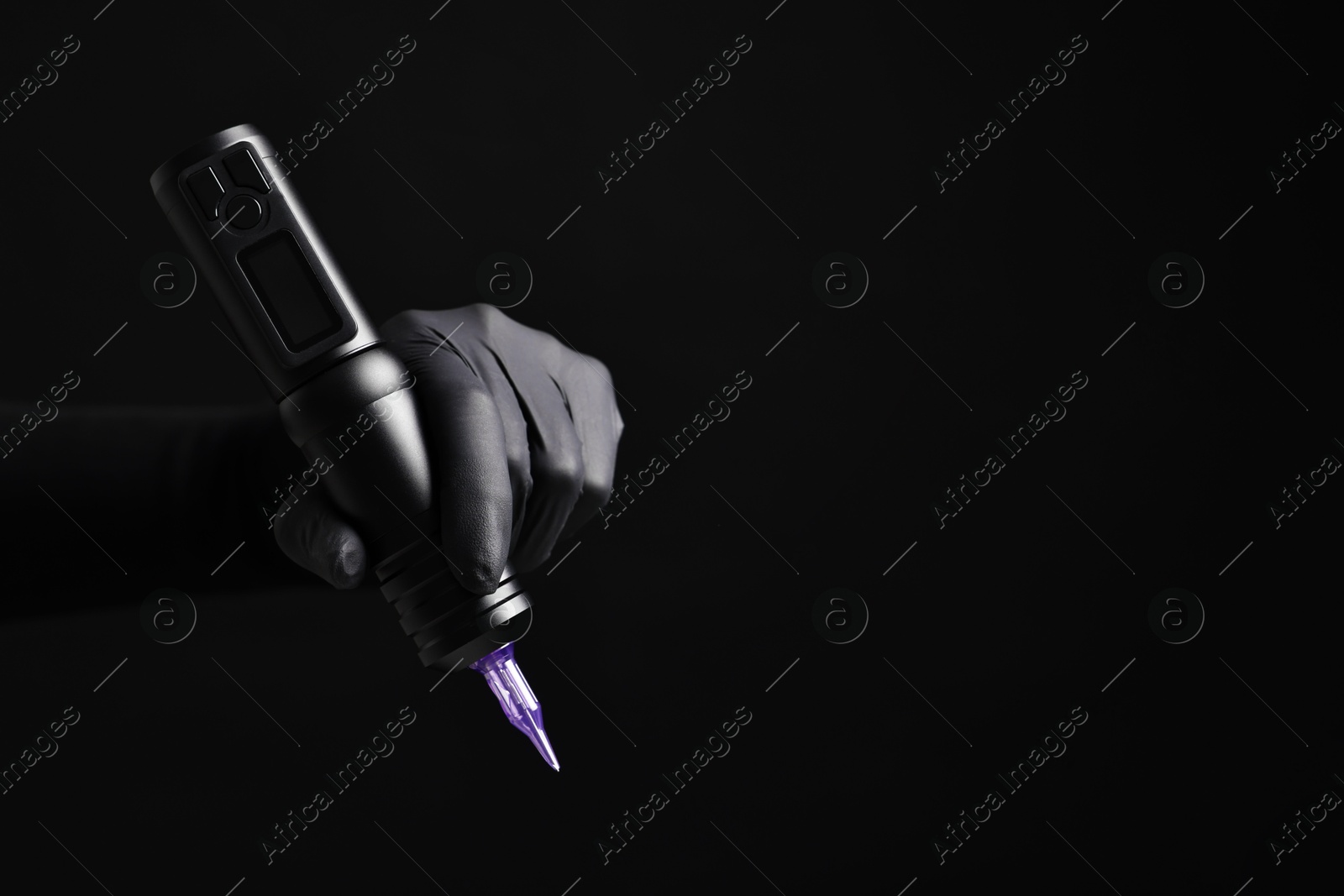 Photo of Professional artist in gloves holding tattoo machine on black background, closeup. Space for text