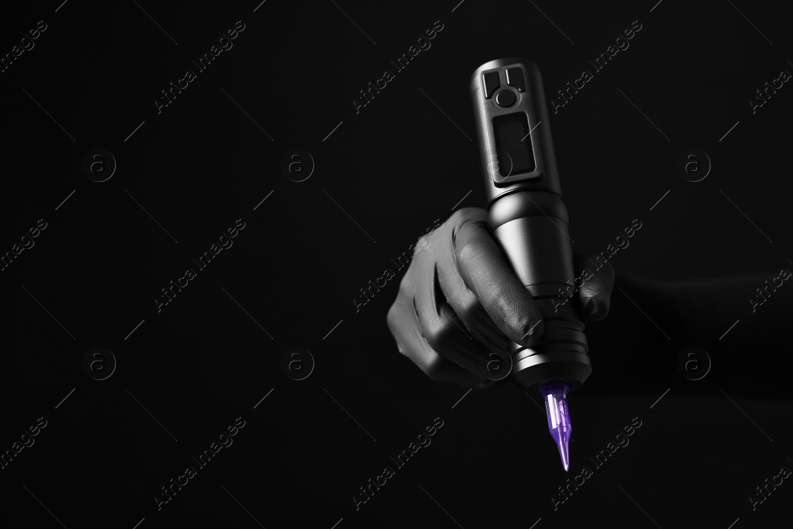 Photo of Professional artist in gloves holding tattoo machine on black background, closeup. Space for text