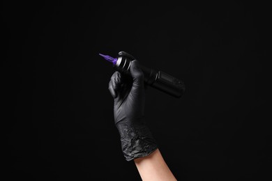 Photo of Professional artist in gloves holding tattoo machine on black background, closeup