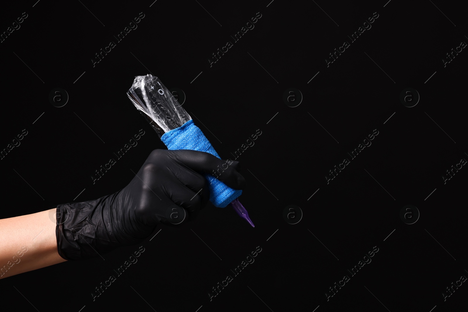 Photo of Professional artist in gloves holding tattoo machine on black background, closeup. Space for text