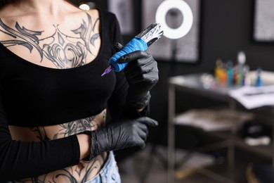 Photo of Professional artist in gloves with tattoo machine in salon, closeup. Space for text