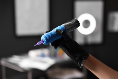 Photo of Professional artist in gloves with tattoo machine in salon, closeup