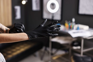 Photo of Professional tattoo artist wearing gloves in salon, closeup. Space for text