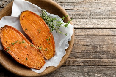 Photo of Halves of tasty cooked sweet potato with thyme on wooden table, top view. Space for text