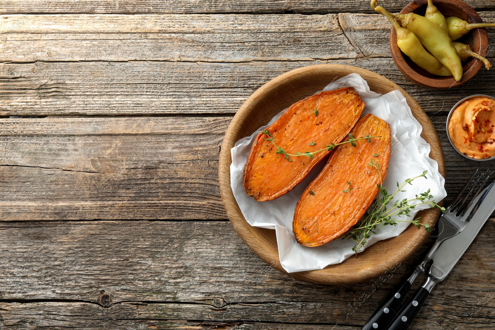 Photo of Tasty cooked sweet potato served with thyme and sauce on wooden table, top view. Space for text