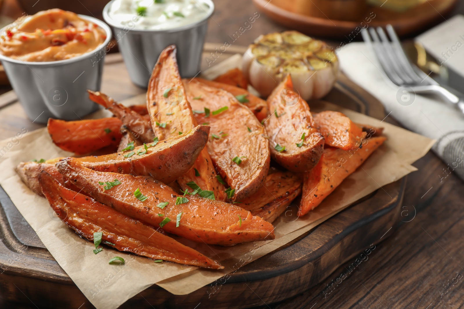 Photo of Tasty cooked sweet potatoes served with sauces on wooden table, closeup