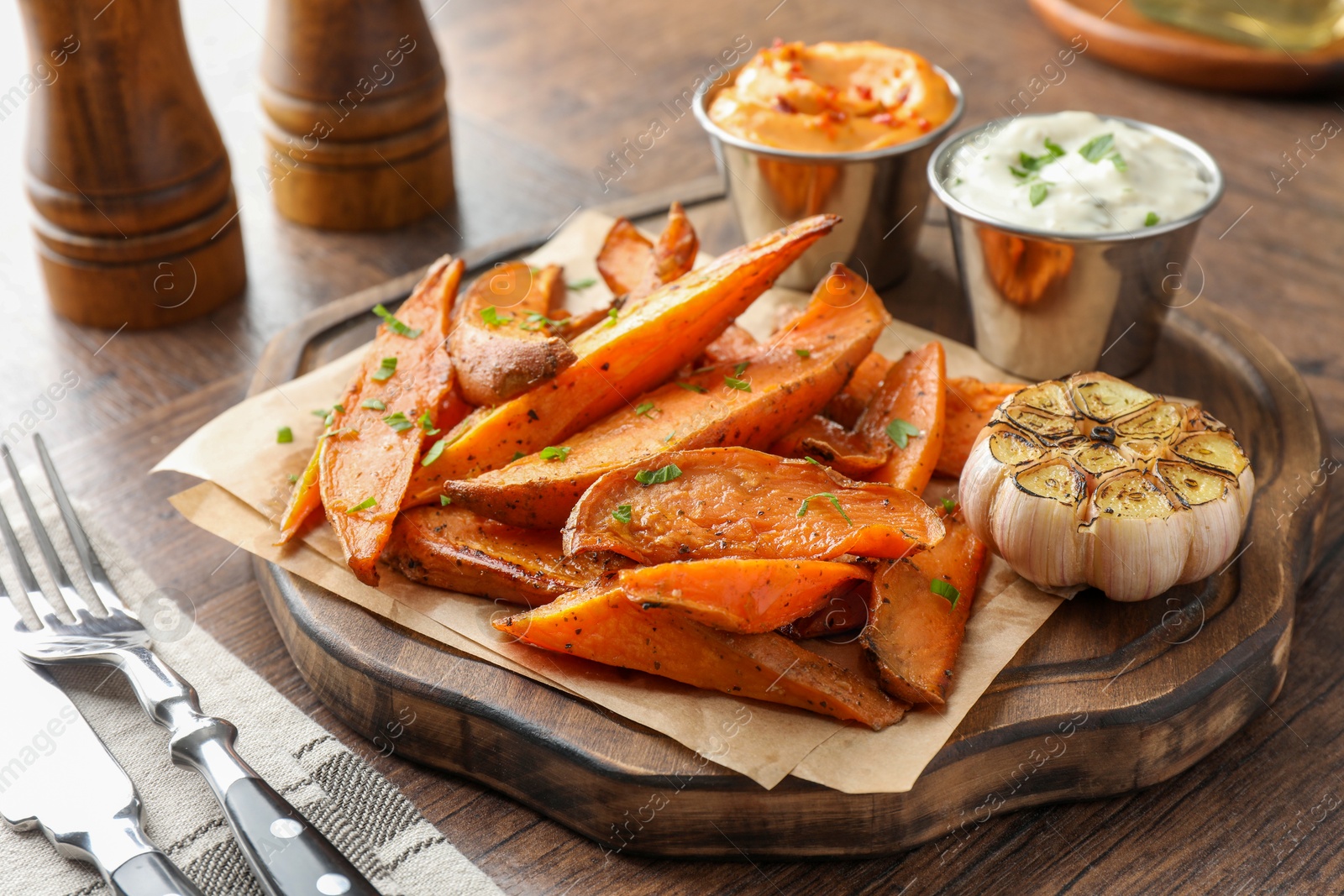 Photo of Tasty cooked sweet potatoes served with sauces on wooden table, closeup