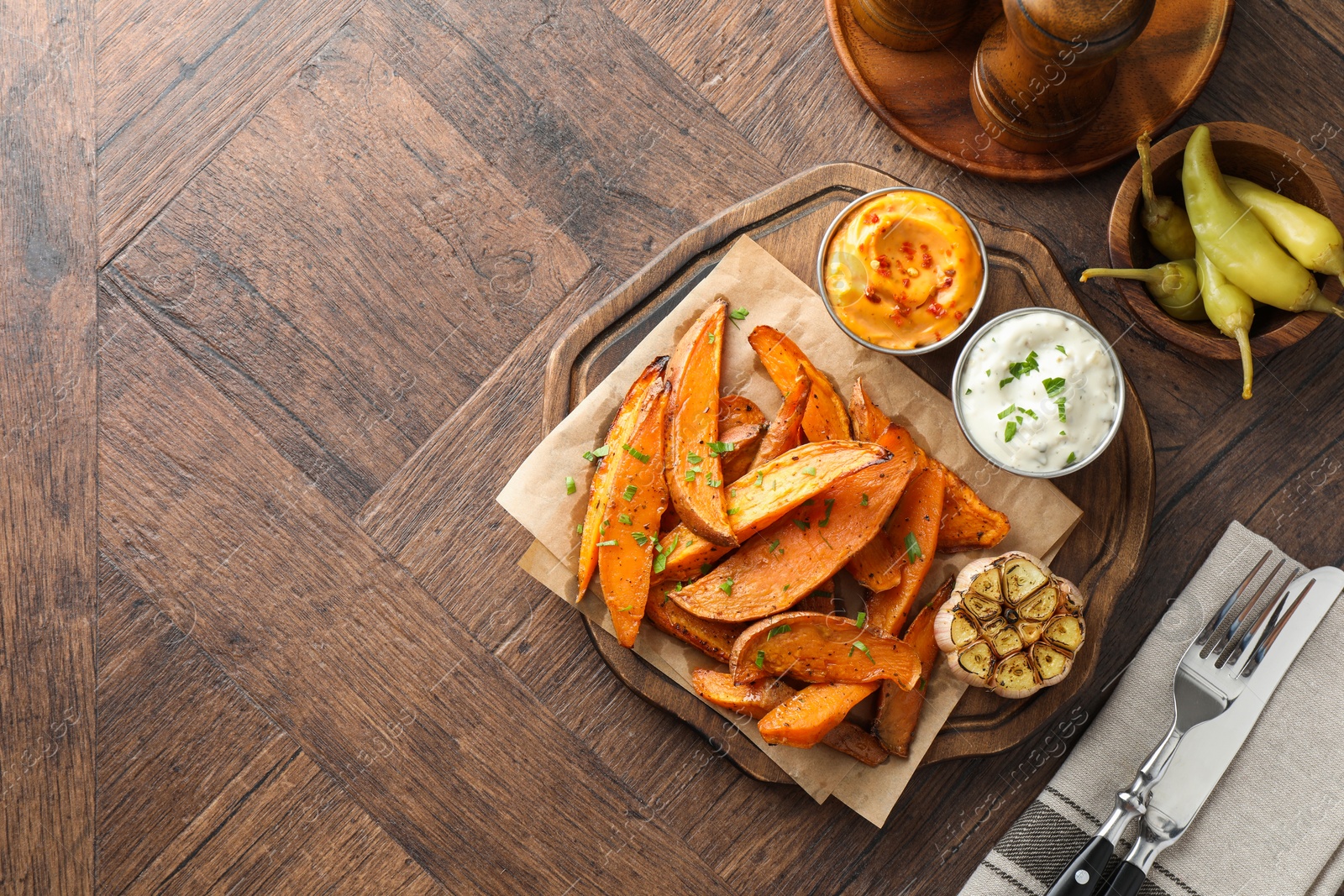 Photo of Tasty cooked sweet potatoes served with sauces on wooden table, top view. Space for text