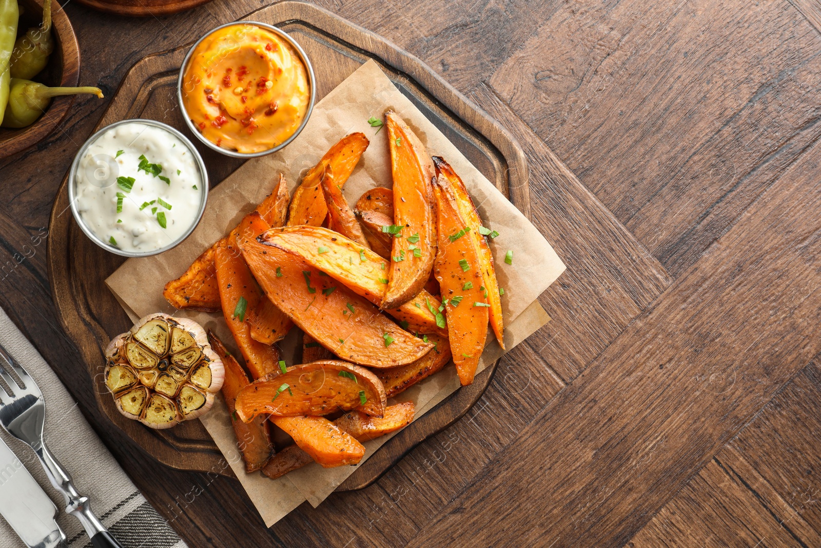 Photo of Tasty cooked sweet potatoes served with sauces on wooden table, top view. Space for text