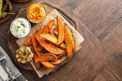 Photo of Tasty cooked sweet potatoes served with sauces on wooden table, top view. Space for text