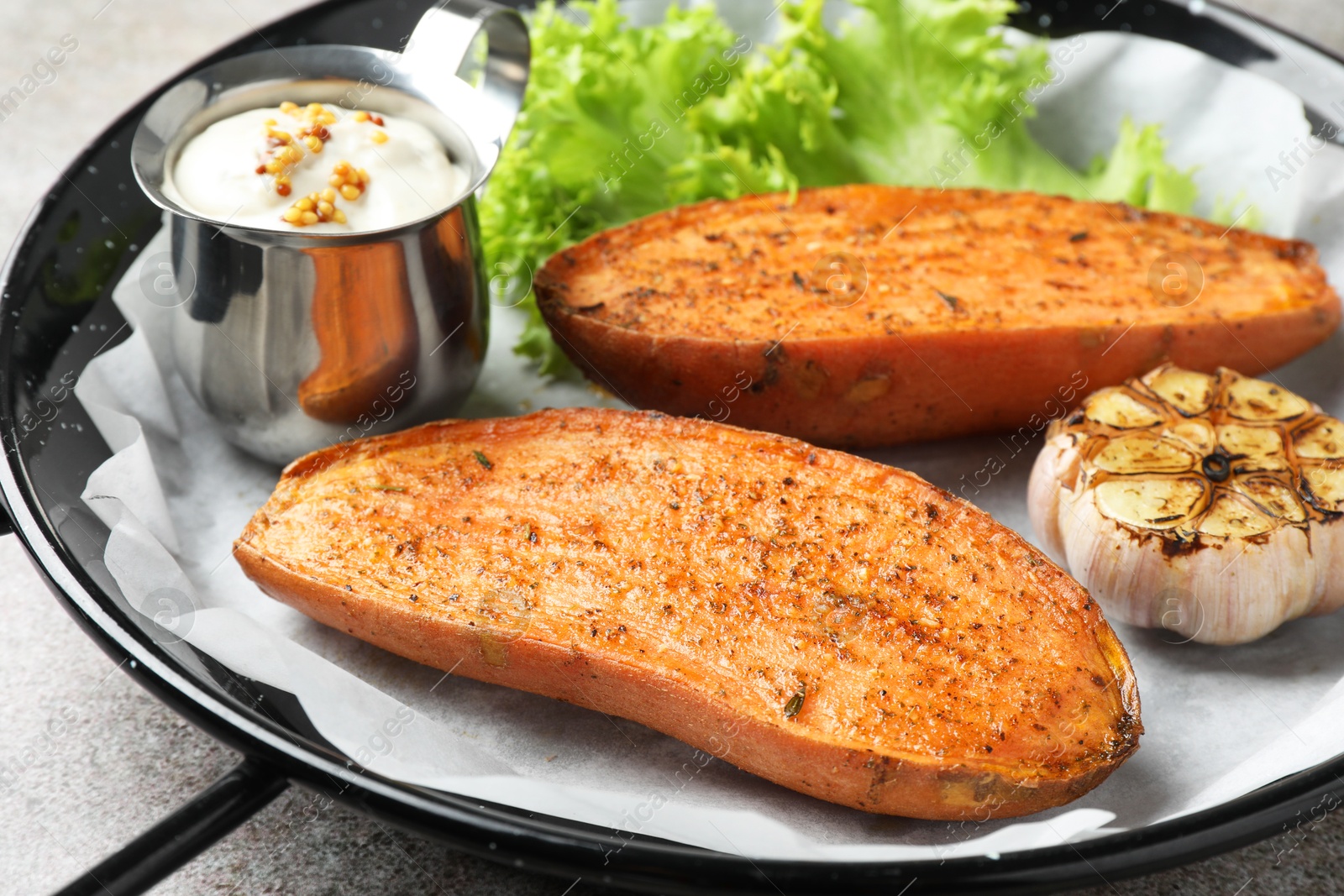 Photo of Tasty cooked sweet potato served in baking dish on grey table, closeup