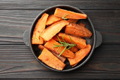 Photo of Pieces of tasty cooked sweet potato with rosemary in baking dish on wooden table, top view