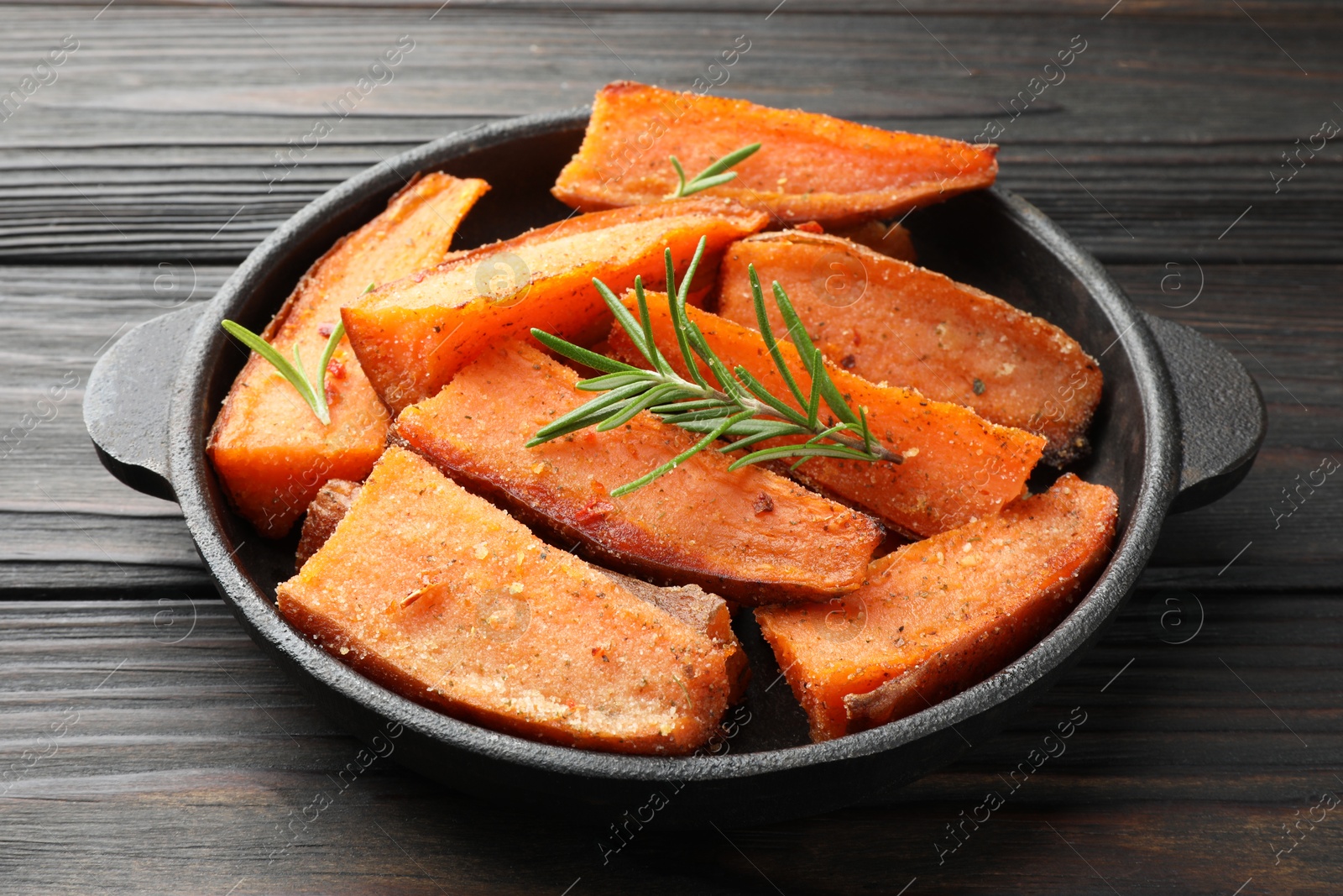 Photo of Pieces of tasty cooked sweet potato with rosemary in baking dish on wooden table, closeup