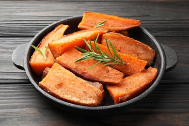 Photo of Pieces of tasty cooked sweet potato with rosemary in baking dish on wooden table, closeup